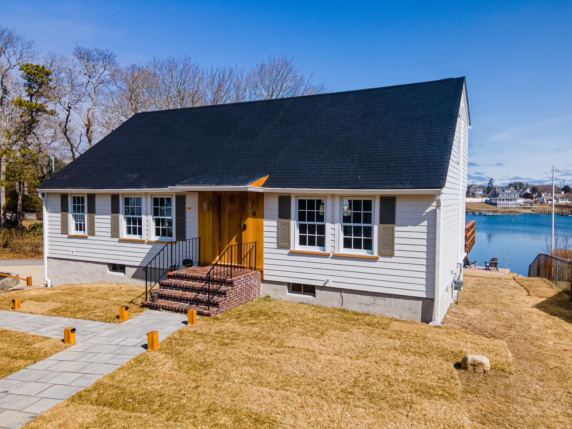 Angled waterfront home exterior with custom wood entry, white siding, refined trim work, and crisp facade details.
