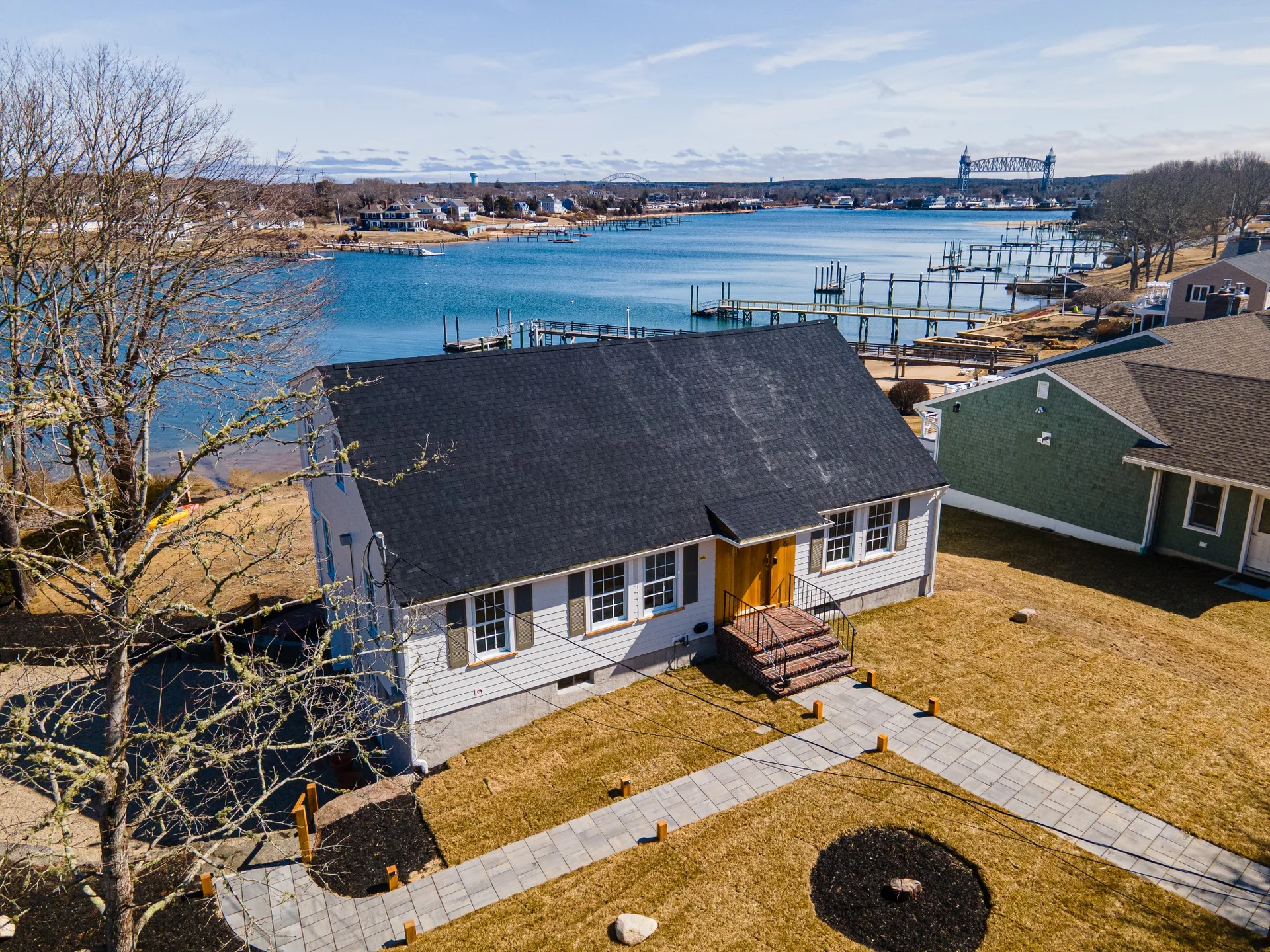 Aerial front view of the completed waterfront home exterior, driveway, property layout, and surrounding landscape.