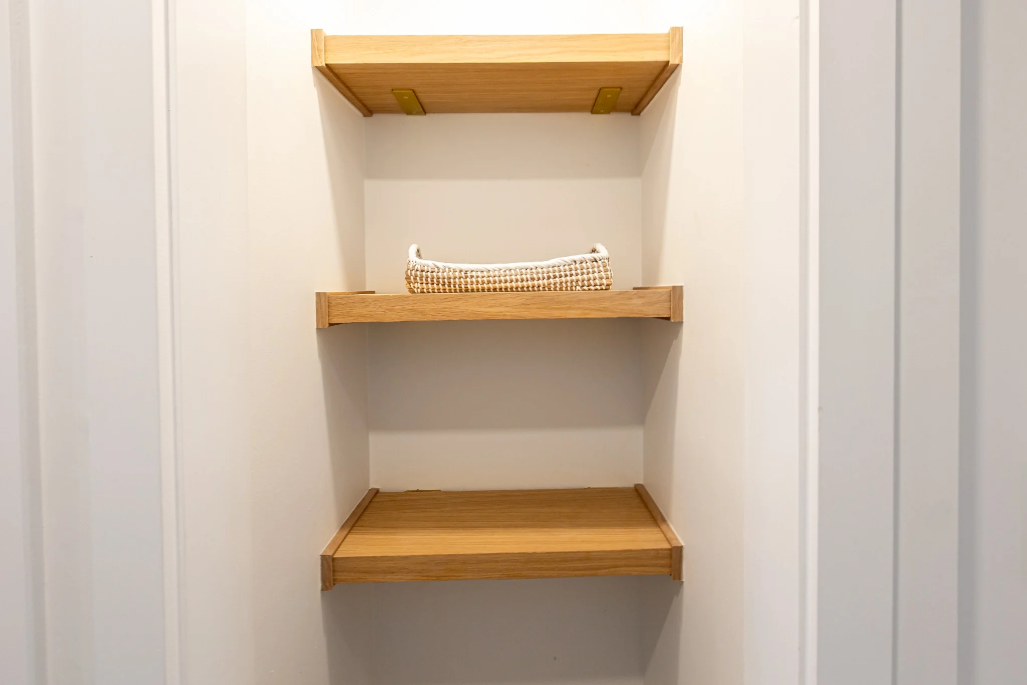 Custom closet shelving detail with three built-in oak shelves in a clean white niche.