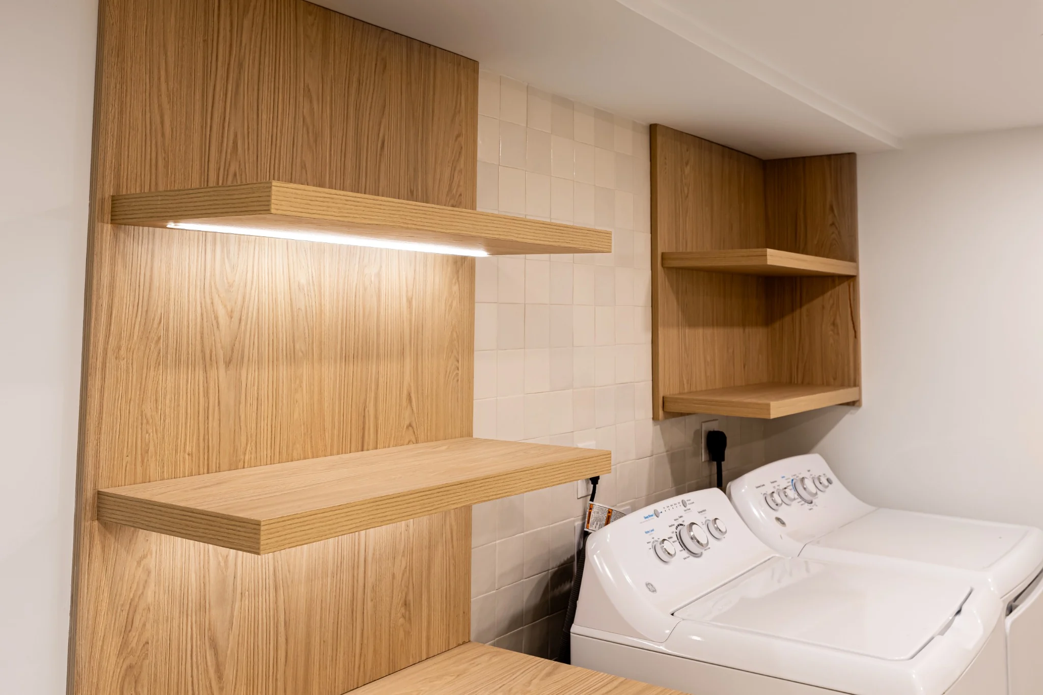 Laundry room custom wood shelving detail with warm oak shelves and clean white wall finish.