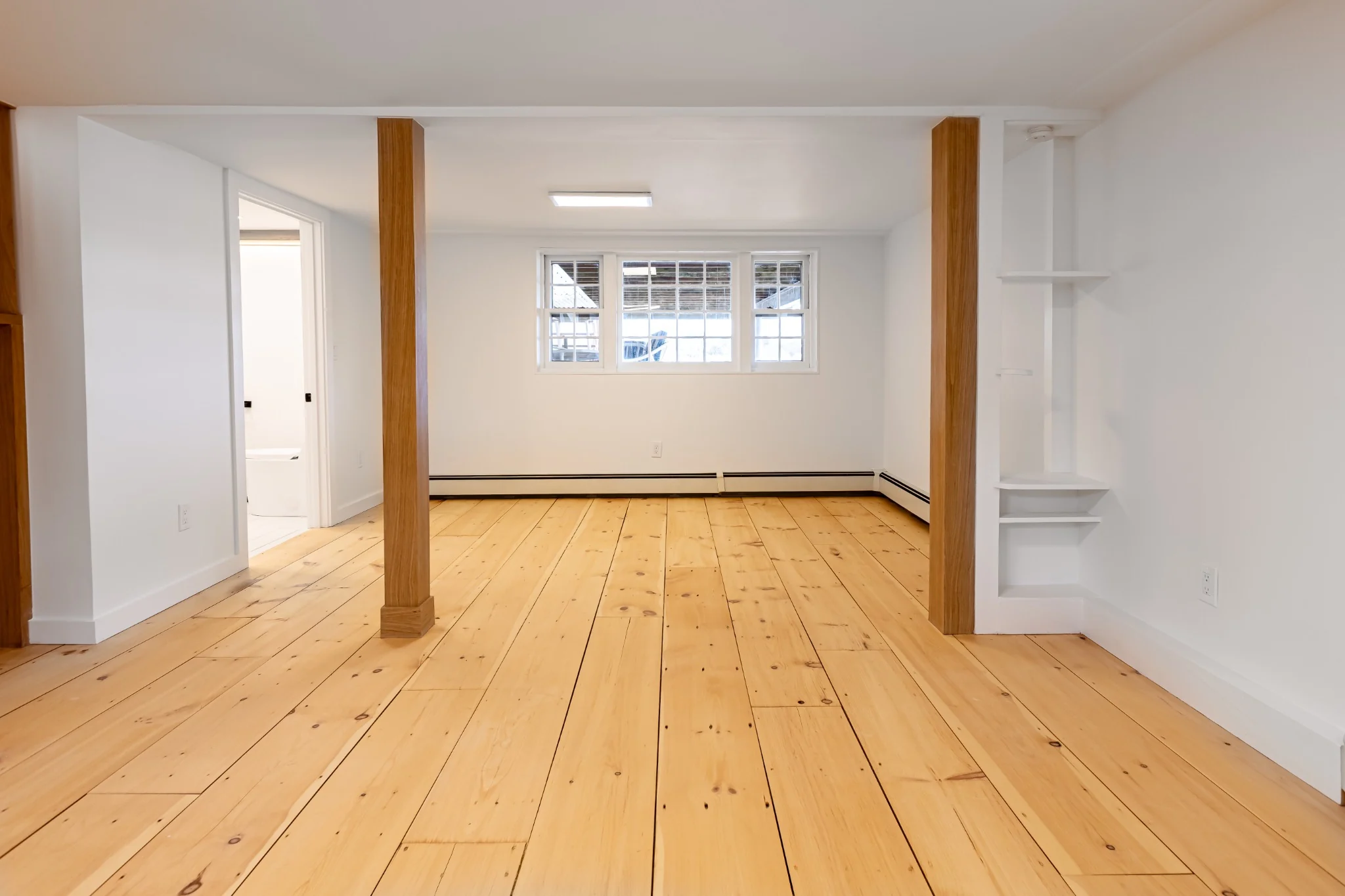 Finished basement with wide plank wood floor, open lower-level layout, exposed wood posts, and clean walls.